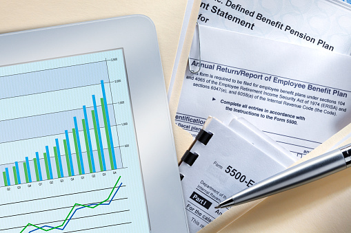 A high angle view of a mobile device that rests on top of a stack of defined benefit documents. A chart and graph are on the mobile device screen.