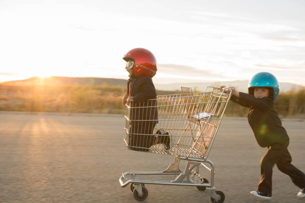 Young Business Boys Racing a Shopping Cart Two young boys dressed as businessmen wearing racing goggles and helmets race a shopping cart on a rural road in Utah, USA. One boy pushes the other business boy while working together towards a finish line. uncertainty photos stock pictures, royalty-free photos & images