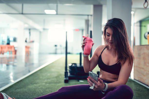 istock Cute Female Drinking Water And Using Phone After Workout IN gym 1169232891