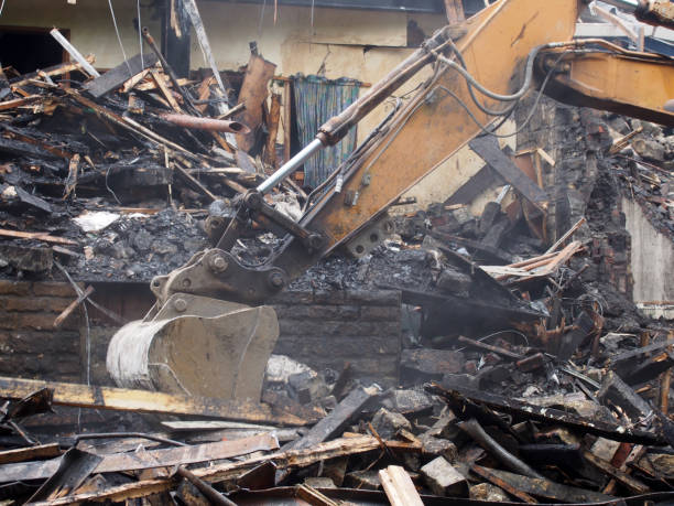istock Hydraulic crusher excavator machinery working on a demolition site clearing burned debris with dust and smoke 1169234133