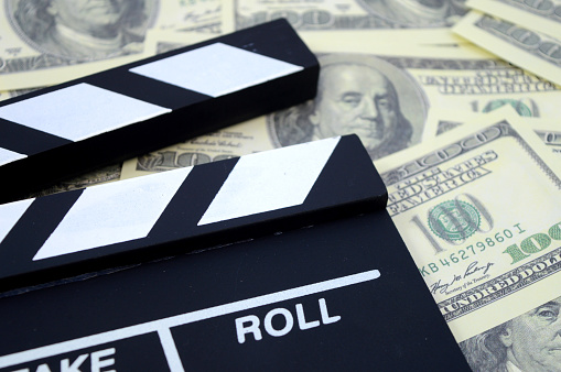 A conceptual image focused on the movie industry and the money it can produce using a clapboard and American cash as a background.