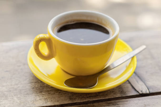 Chipped yellow coffee cup and saucer on a wooden table, Closeup with a shallow depth of field black coffee stock pictures, royalty-free photos & images