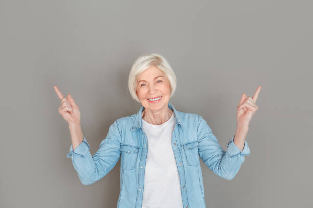 istock Senior woman in jeans jacket studio isolated on grey wall pointing up copyspace 1169246817