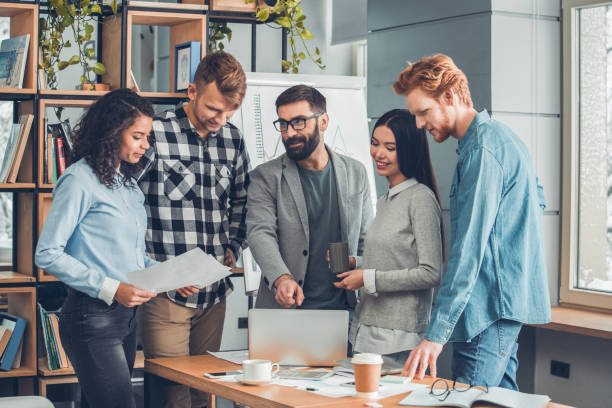 istock Startupers working together at office standing boss pointing at laptop explaining strategy while employees looking at screen smiling joyful 1169246839