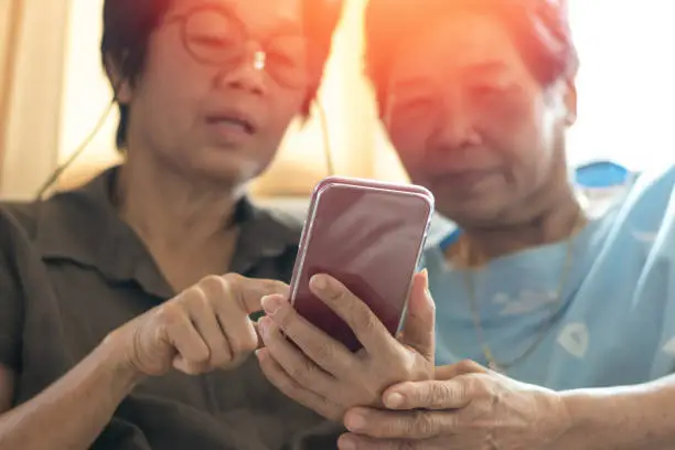 Happy elderly senior people society lifestyle technology concept. Ageing Asia women using tablet smartphone or mobile phone share social media together in wellbeing county home.