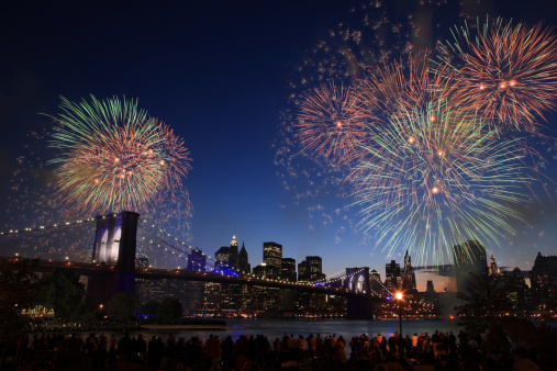 A crowd of people watching fireworks above the Brooklyn Bridge and Manhattan skyline