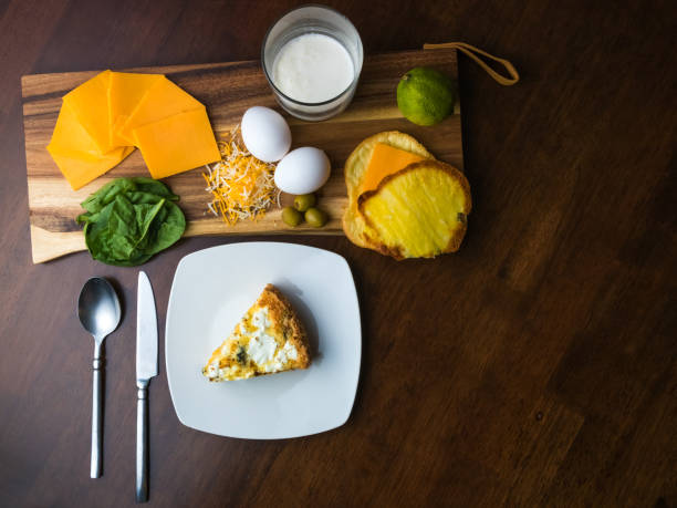 Homemade keto spinach and goat cheese pie cut and plated.  Ingredients from the pie are organized on a wooden chopping block. This wide angle image is viewed from above. Copy space.