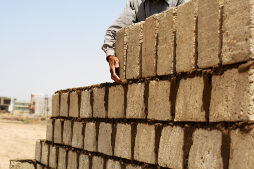 Bottom view of a housebuilder building a house. In foreground is pile of bricks.