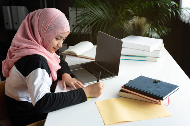 asiática isalamica religiosa adolescente mujer sentarse.trabajar con la computadora portátil en la mesa, fondo de la ventana, con la intención de gustar gusano de libro. educación del conocimiento, estudio duro, concepto de educación. - intend fotografías e imágenes de stock