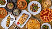 assorted food set on table top view. beef wok noodles, miso soup, gedza, japan rolls, sushi, pizza pepperoni, pizza quatro formaggi.