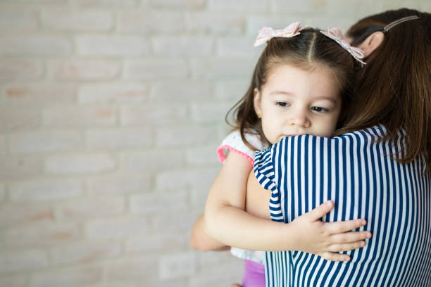 Mother carrying cute little daughter against wall at home