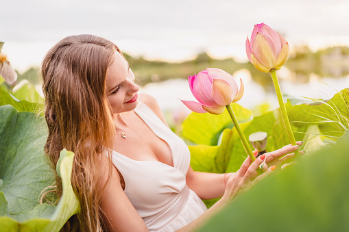 A beautiful young woman stands among the flowering lotus. Portrait
