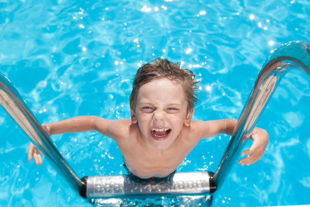 happy delightful small child laughing standing on stainless handrail of turquoise outdoor summer swimming pool during leisure travel - fashionable the human body short hair human head imagens e fotografias de stock