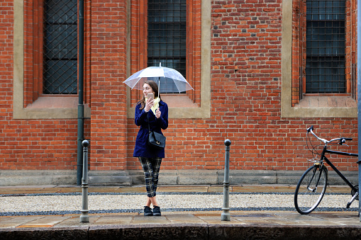 Young woman with umbrella using smart phone and waiting