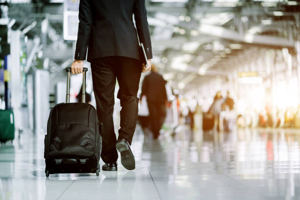 istock Businessman checking e-mail on mobile phone while walking with suitcase inside airport 1169292682