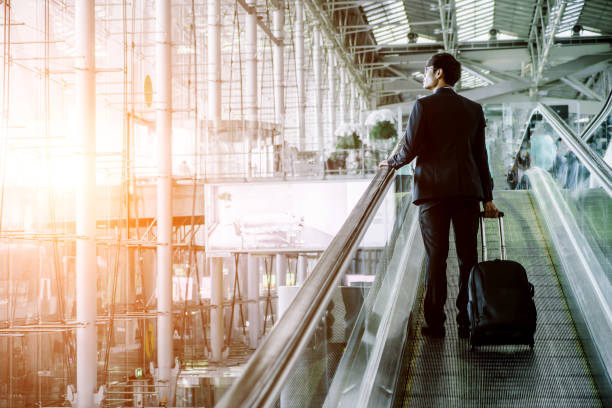 istock Businessman checking e-mail on mobile phone while walking with suitcase inside airport 1169292741