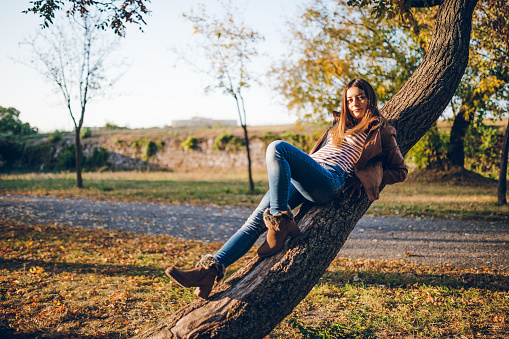 Beautiful young caucasian woman in autumn park sitting on a tree.