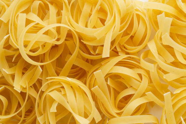 sfondo pasta fatto di nidi di tagliatelle secche non cotti. - pasta noodles tagliatelle freshness foto e immagini stock