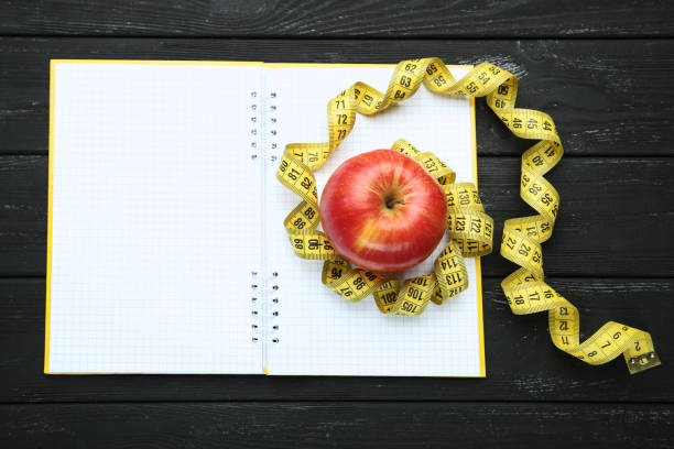 istock Measuring tape with red apple and notepad on wooden table 1169301992