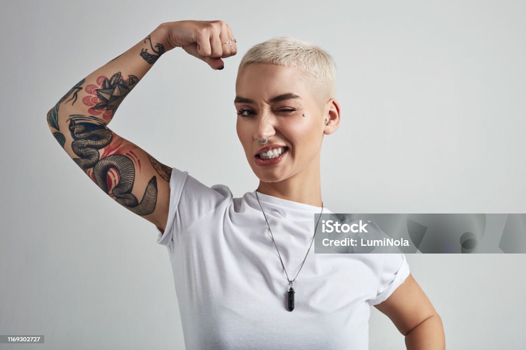 Bringing out the big guns Shot of an attractive young woman flexing her biceps against a grey background Women Stock Photo