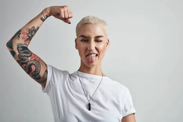 Shot of an attractive young woman flexing her biceps against a grey background