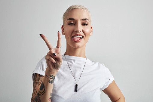 Portrait of an attractive young woman showing the peace sign against a grey background