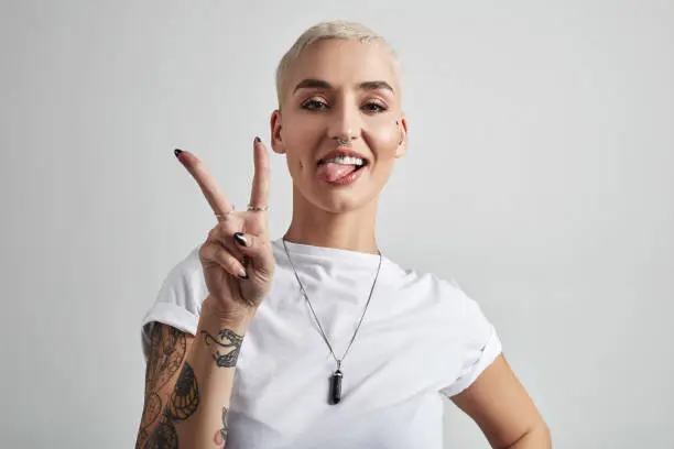 Portrait of an attractive young woman showing the peace sign against a grey background