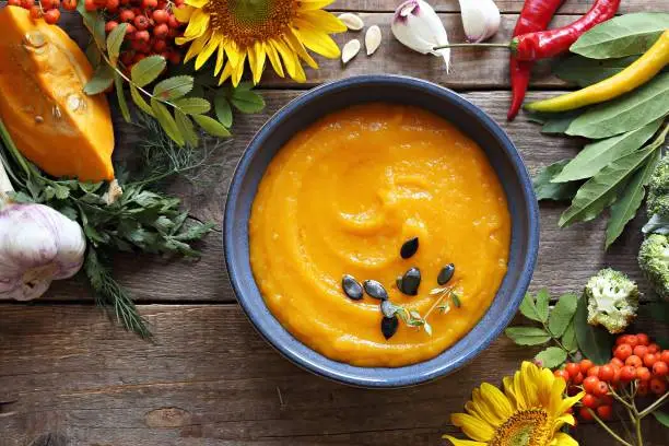 Pumpkin cream soup served on rustic wooden table with ingredients and festive autumn decoration. Overhead view