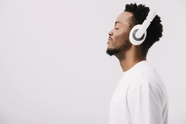 Photo of side view of happy african american man listening music in headphones on white