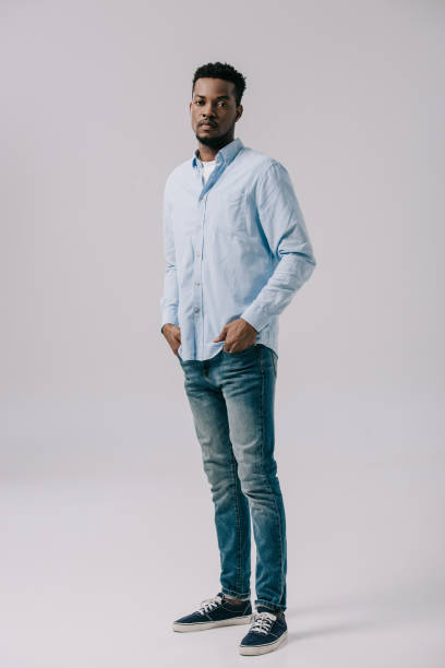 istock handsome african american man standing with hands in pockets on grey 1169310063