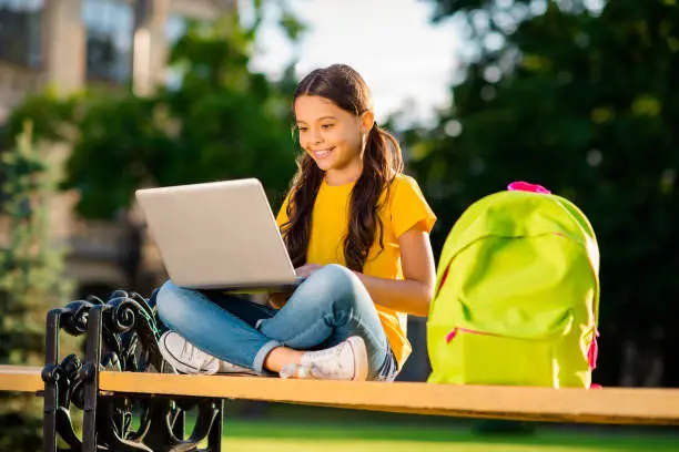 Photo of Portrait of her she nice attractive charming shine lovely cheerful cheery wavy-haired girl sitting on bench chatting online watching interesting lesson in the street park town outside outdoors