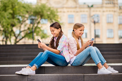 Profile side view of two nice attractive lovely cheerful cheery focused, pre-teen girls chatting online internet browsing app 5g spending day weekend rest relax free time outdoors