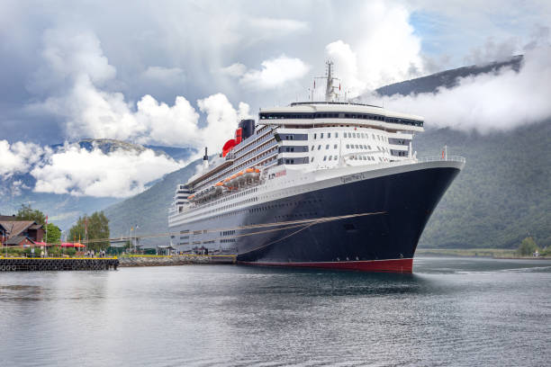 la nave oceanica e bandiera di cunard, queen mary 2, attraccò nello splendido luogo di flam nei fiordi norweigiani circondati da nuvole che pendevano sul paesaggio montano circostante. - queen mary 2 foto e immagini stock