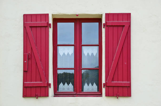 sunny view of a windows of an old farm house with shutters, where a curtain of handmade crochet hangs stock photo