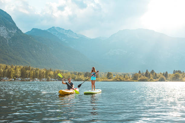 młoda kobieta paddleboarding i młody mężczyzna w kajaku na jeziorze - lake bohinj zdjęcia i obrazy z banku zdjęć