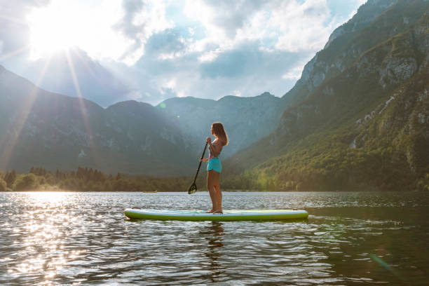 młoda kobieta paddleboarding na jeziorze o zachodzie słońca - lake bohinj zdjęcia i obrazy z banku zdjęć