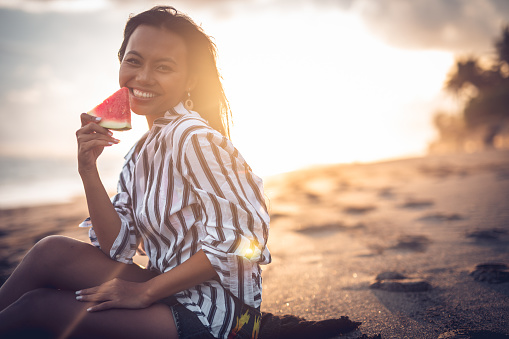One woman, beautiful woman eating watermelon on the beach in sunset alone.