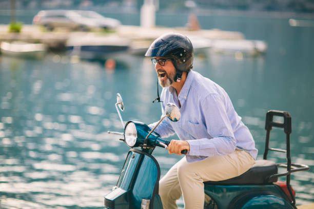 Mature man driving motor scooter in marina near the sea.