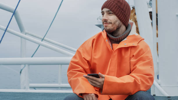 pescador casualy vestido usando o telefone móvel ao viajar no navio. - seine net fotos - fotografias e filmes do acervo