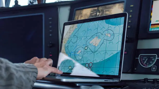 Photo of Captain of Commercial Fishing Ship Surrounded by Monitors and Screens Working with Sea Maps in his Cabin.