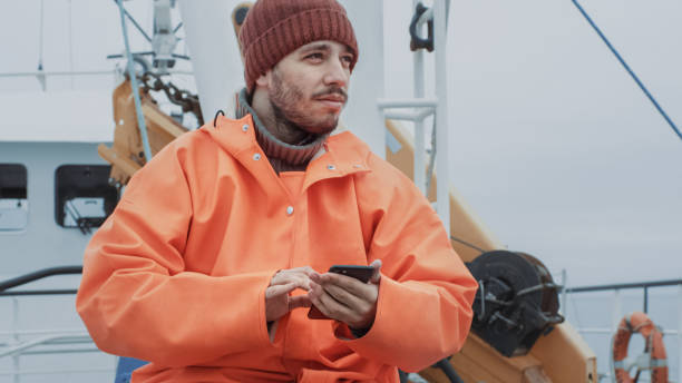 pescador casualy vestido usando o telefone móvel ao viajar no navio. - seine net fotos - fotografias e filmes do acervo