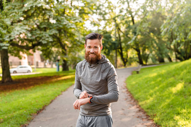 Man checking his watch while exercising in a public park A handsome Swedish man with a beard is exercising in a public park. He is checking his smart watch before and after his run. long sleeved recreational pursuit horizontal looking at camera stock pictures, royalty-free photos & images