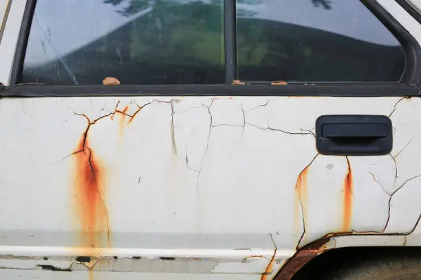 Photo of Details of old peeling paint and rusted white car.