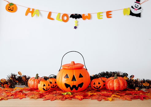 Halloween holiday decoration with pumpkin head jack lantern and autumn leaves on table wood with white wall background, halloween background concept, copy space.