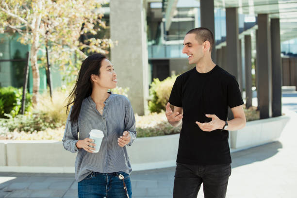 University Students Discussing with Eachother A front-view shot of two multi-ethnic students walking together through a university campus, they are talking to eachother. university students australia stock pictures, royalty-free photos & images