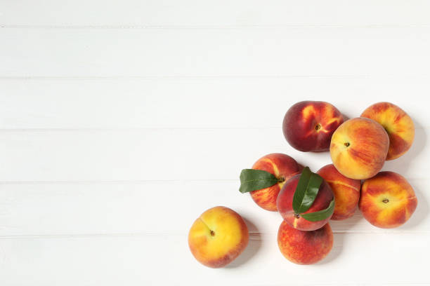 istock Fresh peaches with green leafs on white wooden table 1169334055
