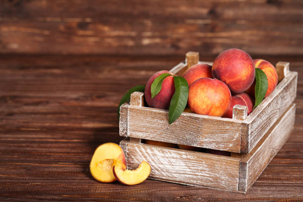 istock Fresh peaches with green leafs in crate on brown wooden table 1169334891