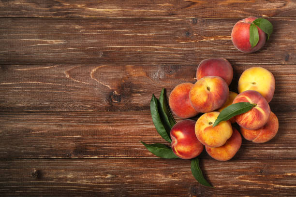 istock Fresh peaches with green leafs on brown wooden table 1169334911