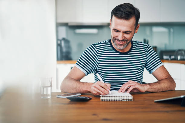 istock Handsome smiling man writing in notebook while managing personal finance 1169340037