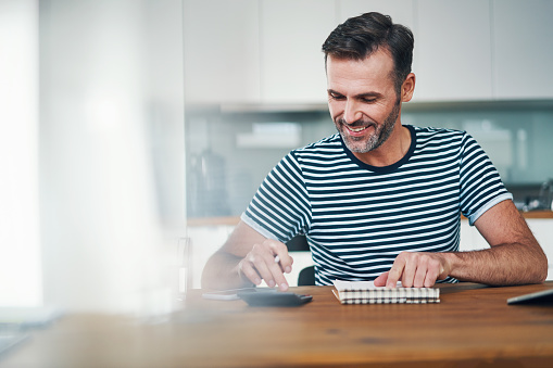 Smiling man using notebook and calculator to manage home budget